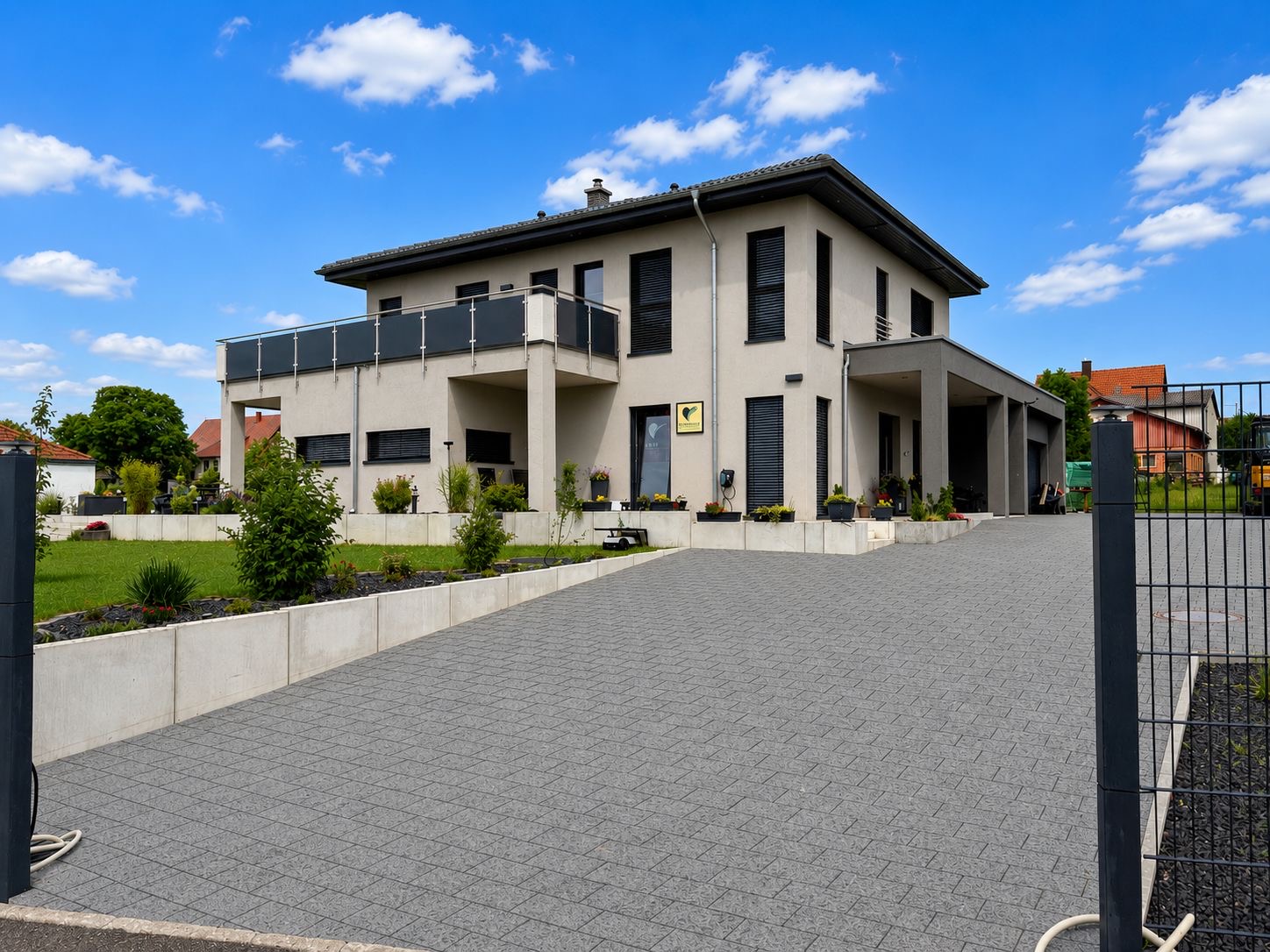 Große gepflasterte Hofeinfahrt in Grau mit Betonmauer-Einfassung und Beetbepflanzung vor einem modernen Wohnhaus